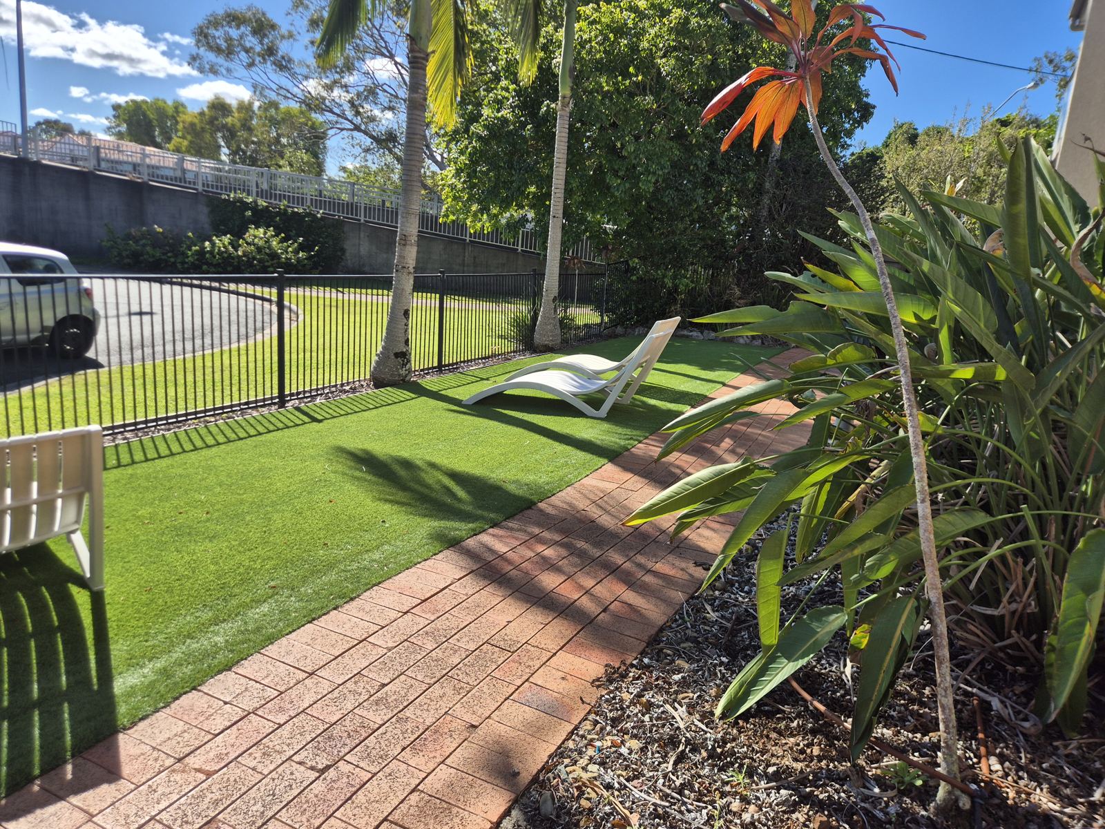 Garden lawn with white sun loungers, palms and a brick path