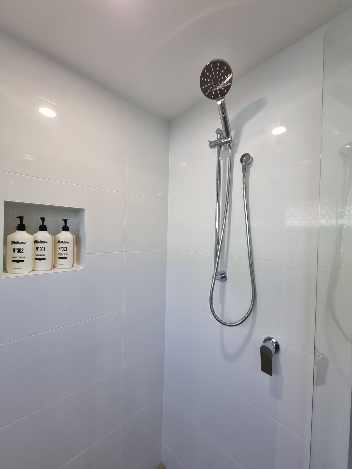 Tiled shower with rail shower head and a niche of Biology shampoo, conditioner and body wash