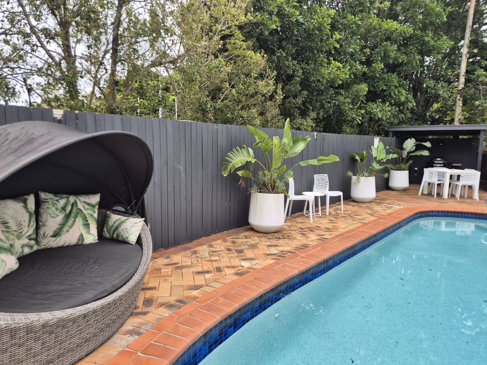 Pool deck with cabana daybed, tropical planters, outdoor seating and covered BBQ area