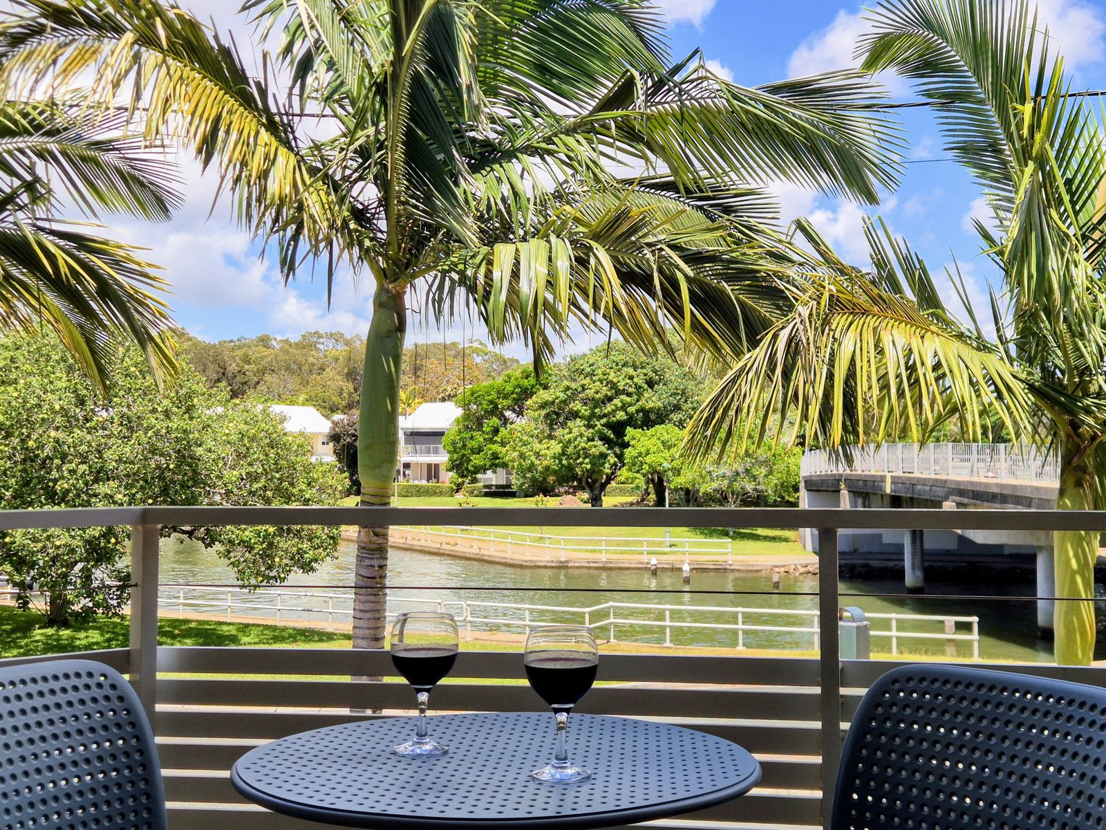 Private balcony with table for two, looking through palms to the canal and bridge