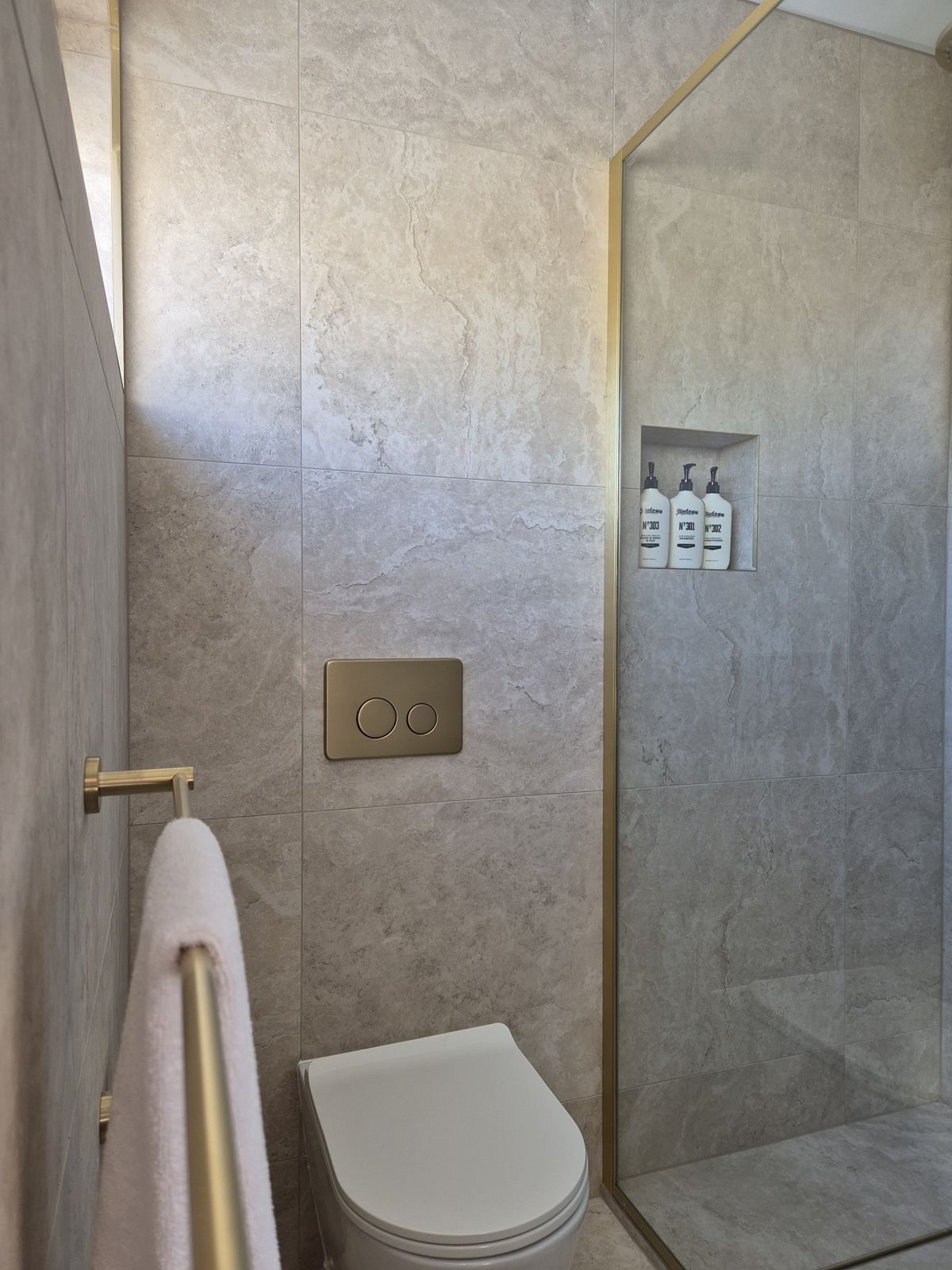 New bathroom with stone-look tiles, brushed brass fittings, frameless shower and Biology Smart Skincare products