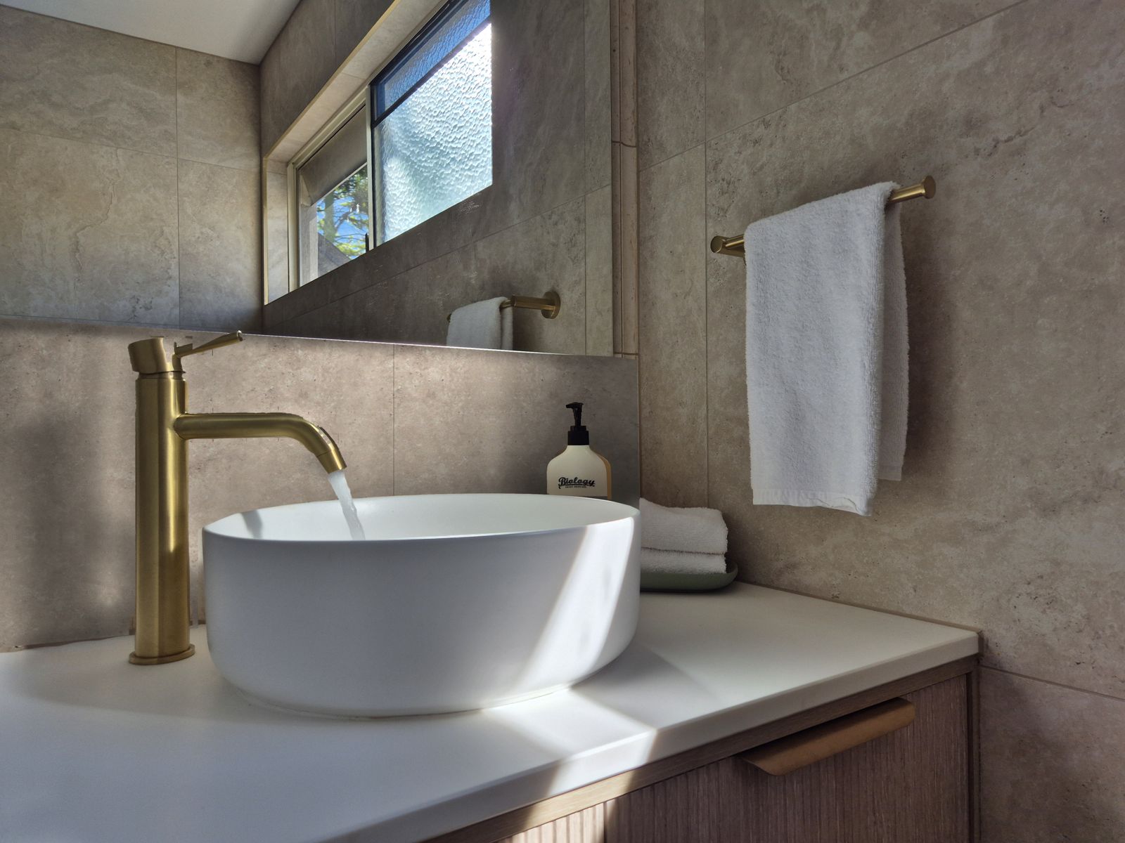 Bathroom vanity with round basin, brushed brass tapware and stone-look tiles