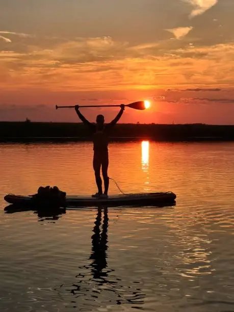 Paddle boarder silhouetted at sunset, paddle raised overhead